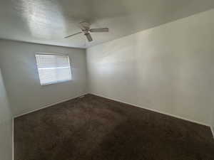 Unfurnished room featuring dark colored carpet and ceiling fan