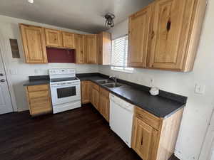 Kitchen with dark countertops, white appliances, dark wood-style floors, and wood finish cabinets