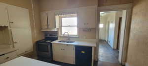 Kitchen featuring stainless steel range with electric stovetop, light countertops, dishwasher, white cabinetry, and a textured wall