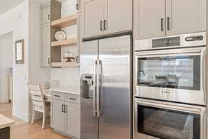 Kitchen featuring stainless steel appliances, open shelves, light wood finished floors, light stone counters, and gray cabinetry