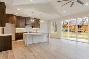 Kitchen featuring decorative light fixtures, a kitchen island with sink, a breakfast bar, vaulted ceiling, and light wood-style flooring
