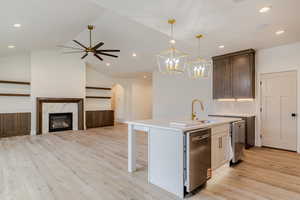 Kitchen with ceiling fan, open floor plan, a high end fireplace, an island with sink, and light wood-type flooring