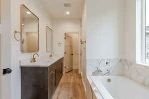 Bathroom with double vanity, recessed lighting, light wood-style floors, and a garden tub