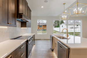 Dual tone kitchen featuring range with electric stovetop, dishwasher, hanging lights, two tone color scheme, and light wood-style flooring