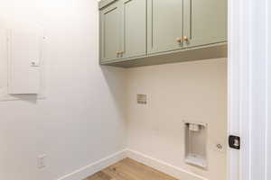 Laundry area with electric panel, light wood-type flooring, cabinet space, and hookup for a washing machine