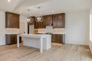 Kitchen featuring tasteful backsplash, two tone cabinetry, a breakfast bar, a kitchen island with sink, and suspended lighting