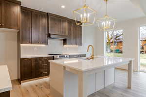 Dual tone kitchen featuring decorative backsplash, dual tone cabinetry, light stone countertops, an island with sink, and light wood-style floors