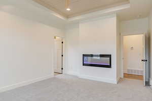 Unfurnished living room with a glass covered fireplace, a wooden tray ceiling, light carpet, and recessed lighting