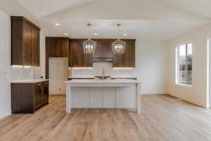 Kitchen featuring tasteful backsplash, an island with sink, pendant lighting, light stone countertops, and two tone cabinetry