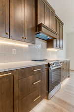 Kitchen featuring stainless steel range with electric stovetop, decorative backsplash, light wood finished floors, and light stone counters