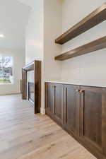 Bar with open shelves, dark wood finish cabinetry, light wood finished floors, and a tiled fireplace