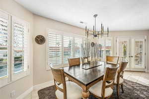 Dining room with light tile patterned flooring, french doors, suspended lighting, and a textured ceiling