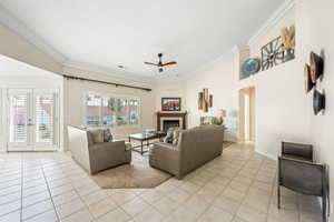 Living room featuring french doors, a ceiling fan, crown molding, a fireplace, and light tile patterned floors