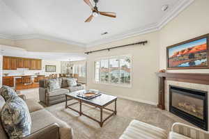 Living room with a ceiling fan, ornamental molding, a fireplace, light colored carpet, and vaulted ceiling