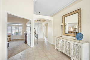 Hallway with arched walkways, light carpet, light tile patterned floors, and ornamental molding