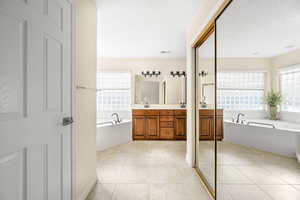 Bathroom featuring a garden tub, double vanity, light tile patterned floors, and a textured ceiling