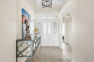 Foyer featuring light tile patterned flooring, ornamental molding, a high ceiling, and arched walkways
