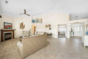 Living area with crown molding, ceiling fan, light tile patterned floors, a fireplace, and arched walkways