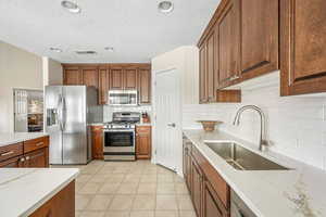 Kitchen with stainless steel appliances, wood finish cabinets, light tile patterned flooring, recessed lighting, and a textured ceiling
