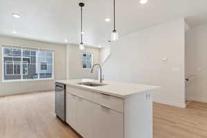 Kitchen featuring pendant lighting, light wood-style floors, white cabinets, and a kitchen island with sink