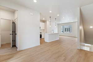 Kitchen with white cabinetry, light countertops, a center island with sink, hanging light fixtures, and light wood-style flooring
