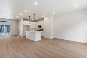 Kitchen with open floor plan, white cabinetry, pendant lighting, a kitchen island with sink, and stainless steel appliances