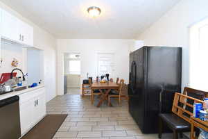 Kitchen featuring black fridge, white cabinets, stainless steel dishwasher, and a textured ceiling