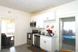 Kitchen featuring stainless steel appliances, white cabinets, light countertops, a textured ceiling, and wood finish floors