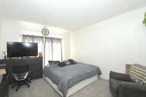Bedroom featuring a textured ceiling, light carpet, and a desk