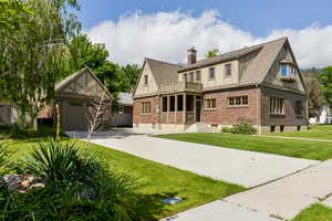Tudor house with brick siding, driveway, a front lawn, a shingled roof, and a chimney