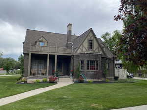 View of front of home with covered porch, brick siding, a front yard, a shingled roof, and a chimney