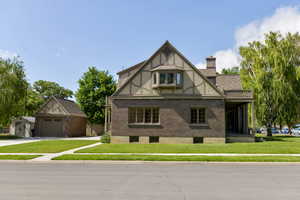 Tudor home with brick siding, an outbuilding, a front lawn, and a chimney