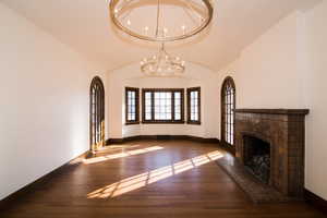 Unfurnished living room featuring wood finished floors, a fireplace with raised hearth, hanging lights, and lofted ceiling