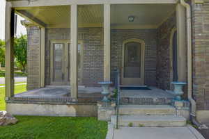 Entrance to property with a porch and brick siding