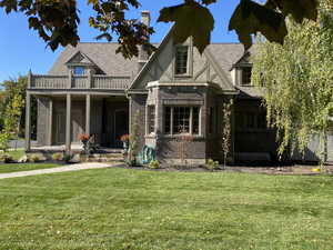 Tudor house featuring a porch, brick siding, a front yard, and roof with shingles