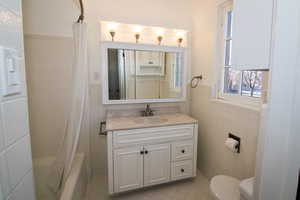 Full bath featuring vanity, tile walls, a wainscoted wall, shower / bath combo, and light tile patterned floors