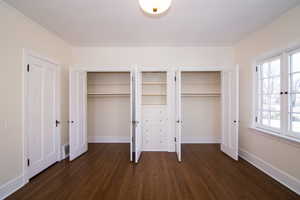 Unfurnished bedroom with two closets and dark wood-style floors