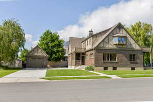 Tudor home with brick siding, a front lawn, an outbuilding, a chimney, and a garage