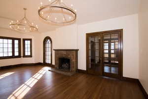 Unfurnished living room featuring french doors, dark wood finished floors, lofted ceiling, a tiled fireplace, and a chandelier