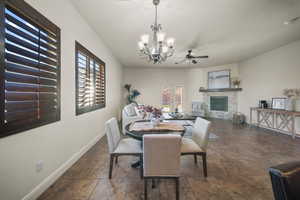 Dining space with a chandelier, ceiling fan, a stone fireplace, dark stone finish flooring, and french doors