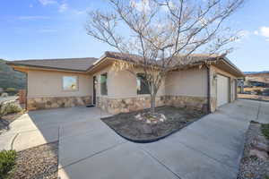 Ranch-style house featuring stucco siding, stone siding, an attached garage, and driveway