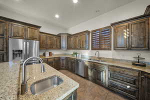 Kitchen with dark wood finish cabinetry, stainless steel appliances, light stone counters, and recessed lighting