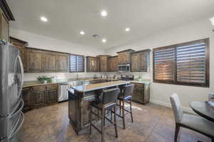 Kitchen with stainless steel appliances, dark wood finish cabinets, light stone counters, a kitchen bar, and a kitchen island
