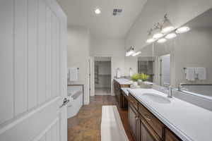 Full bath with two vanities, a spacious closet, stone finish flooring, a garden tub, and recessed lighting