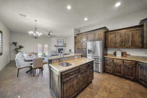 Kitchen with open floor plan, a fireplace, dark wood finish cabinetry, stainless steel fridge, and a center island with sink