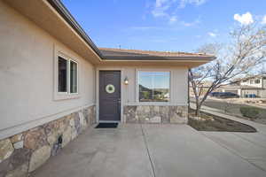Property entrance featuring stucco siding, stone siding, and a patio area