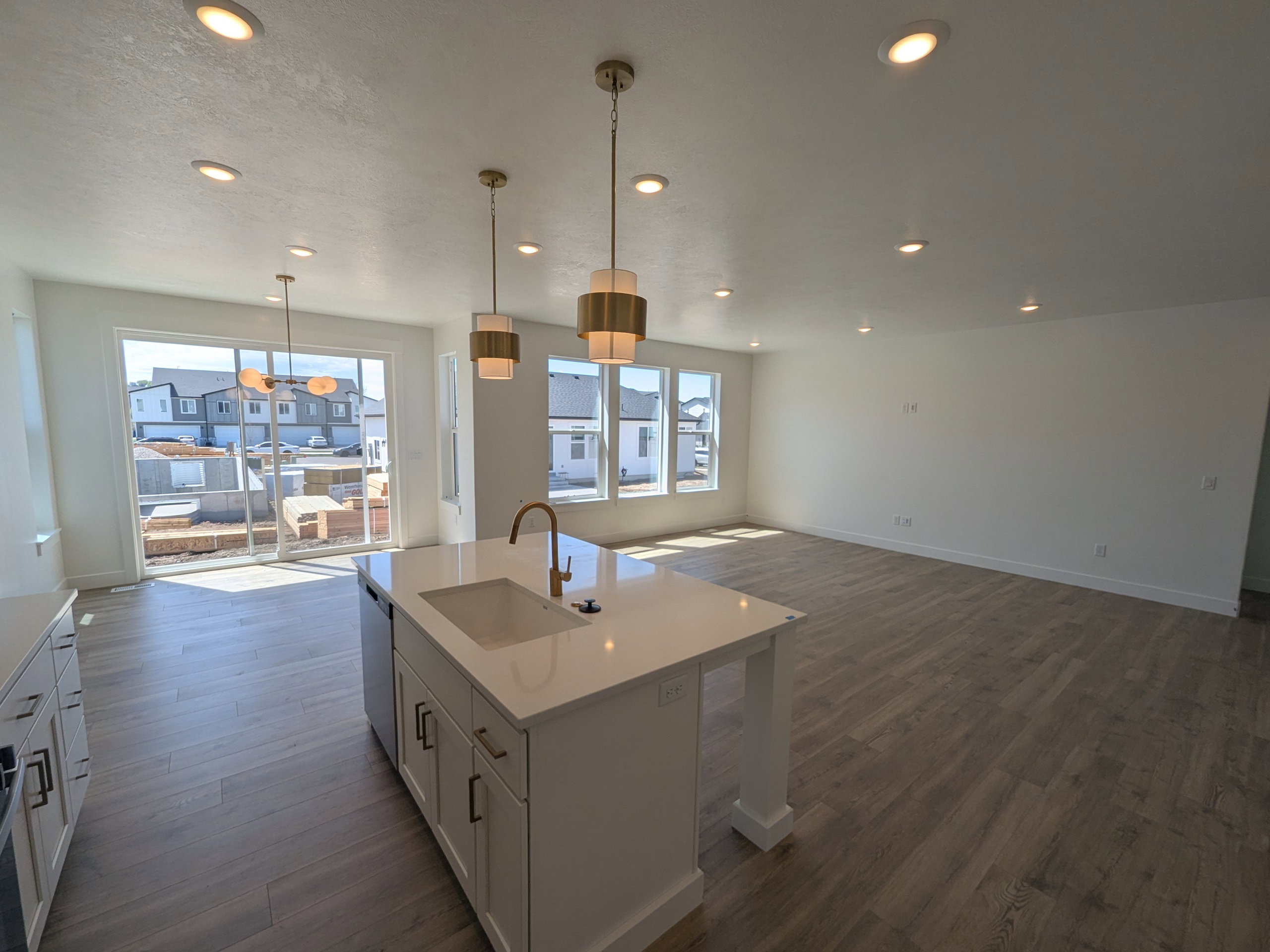 Kitchen featuring open floor plan, a kitchen island with sink, white cabinets, decorative light fixtures, and dark wood-style flooring