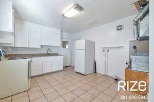 Kitchen featuring white appliances, white cabinetry, decorative backsplash, heating unit, and light stone countertops