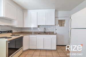Kitchen with white appliances, white cabinetry, decorative backsplash, light stone countertops, and light tile patterned floors