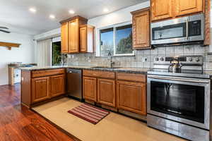 Kitchen with stainless steel appliances, a peninsula, wood finish cabinets, backsplash, and light wood-style flooring